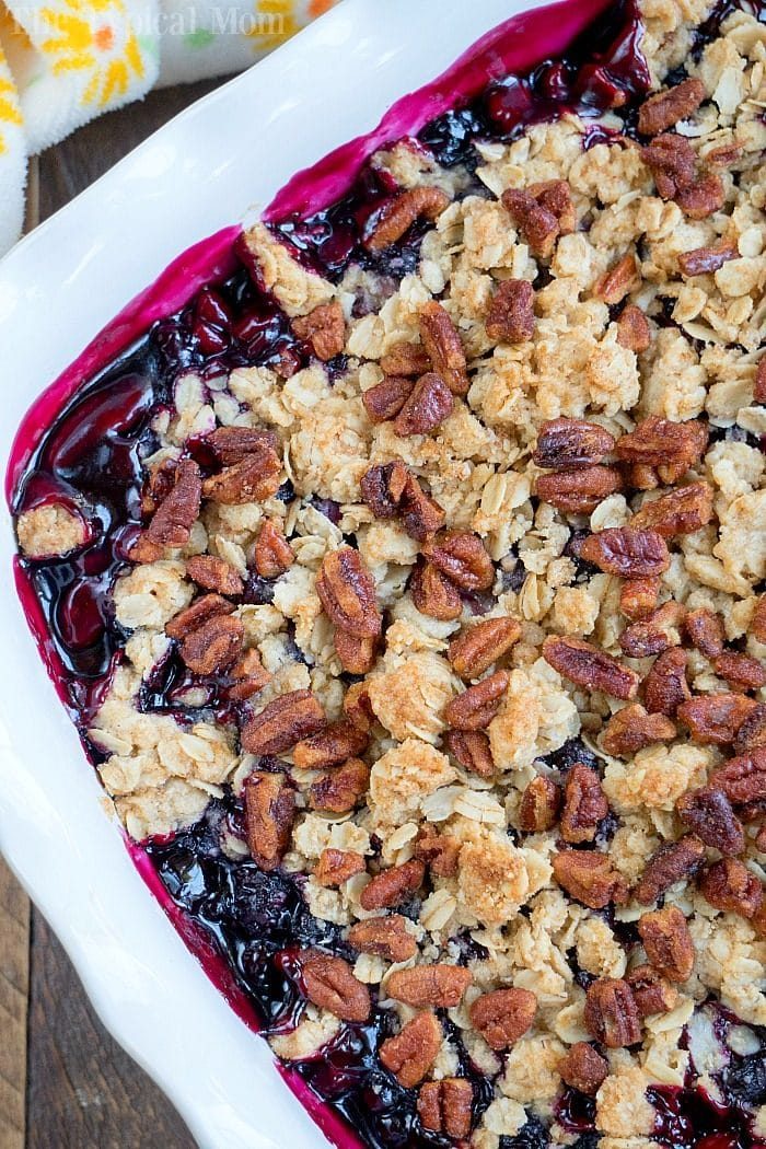 huckleberry crisp topped with oats and pecans in a white baking dish, with a bright purple fruit filling reminiscent of huckleberry cobbler.