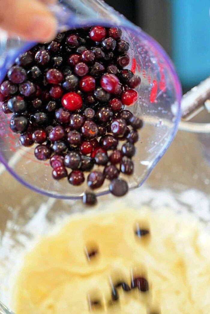 Pouring fresh huckleberries into a mixing bowl with batter, this delightful blend is reminiscent of cherished huckleberry recipes.