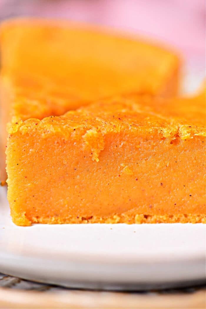 A close-up of a thick slice of orange sweet potato pie on a white plate, reminiscent of the creamy texture found in Impossible Pumpkin Pie.
