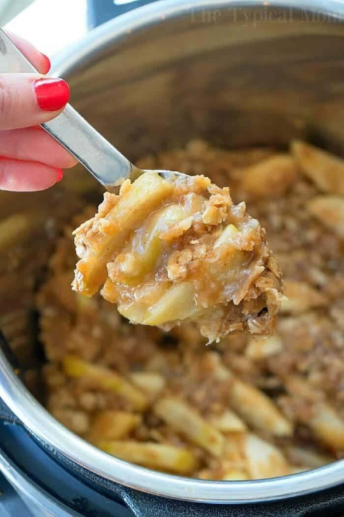 A spoon scoops out warm instant pot apple crisp, revealing tender apples and a golden oat topping.