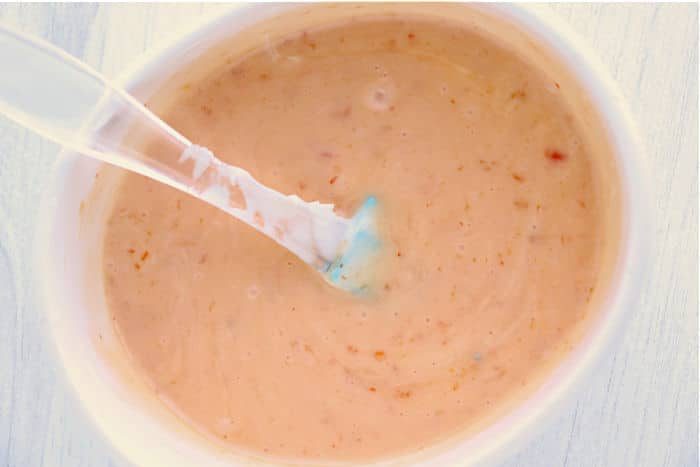 Close-up of a creamy bang bang shrimp sauce with specks, solid for drizzling over instant pot bang bang shrimp, served in a white bowl with a spoon.