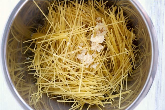 Spaghetti noodles and minced garlic mingle effortlessly in the instant pot, creating a delightful base solid for pairing with tangy bang bang shrimp.