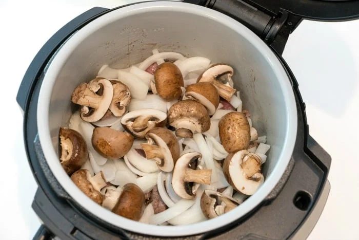 Sliced mushrooms and onions inside an open electric pressure cooker, solid for making flavorful instant pot beef tips.