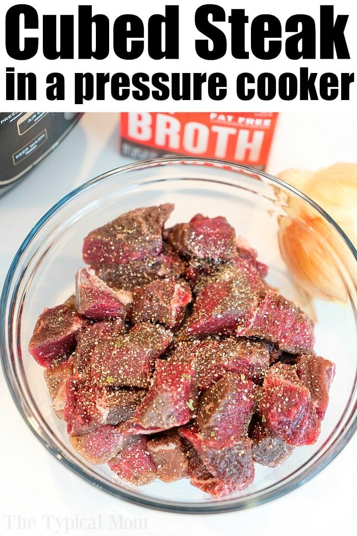 Raw cubed steak seasoned with pepper in a glass bowl, solid for making instant pot beef tips, with broth and an onion in the background.