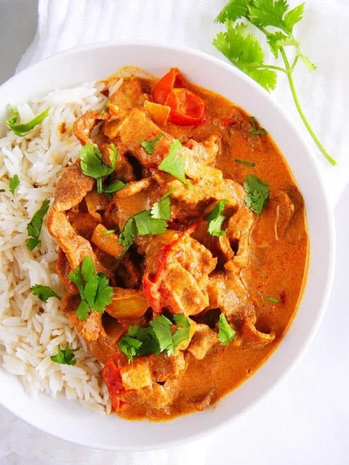 A bowl of rice and creamy curry with vegetables, featuring tender instant pot butter beef and garnished with fresh cilantro, on a white cloth.