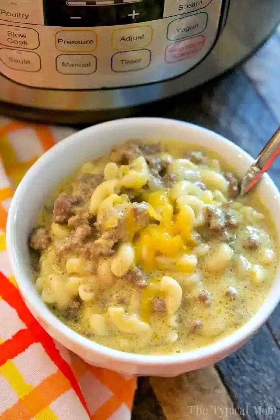 Bowl of Instant Pot cheeseburger macaroni with a spoon, next to an Instant Pot and a colorful napkin.