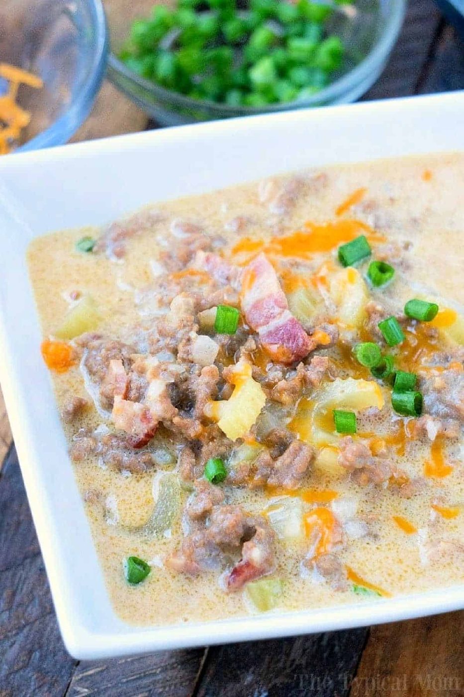 Creamy instant pot cheeseburger soup in a white bowl, topped with ground beef, crispy bacon, melty cheese, and chopped green onions.