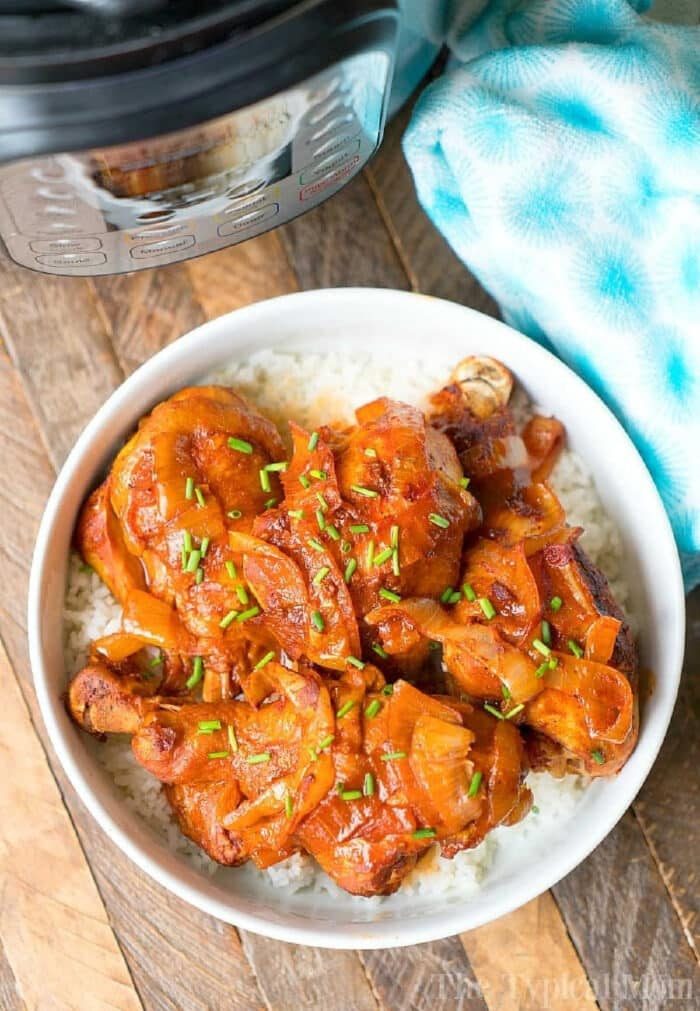 A bowl of rice topped with saucy instant pot chicken legs and chopped chives sits next to an electric pressure cooker.