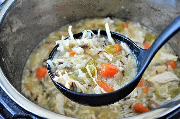 A ladle of Instant Pot chicken rice soup with carrots and celery held over a pot.