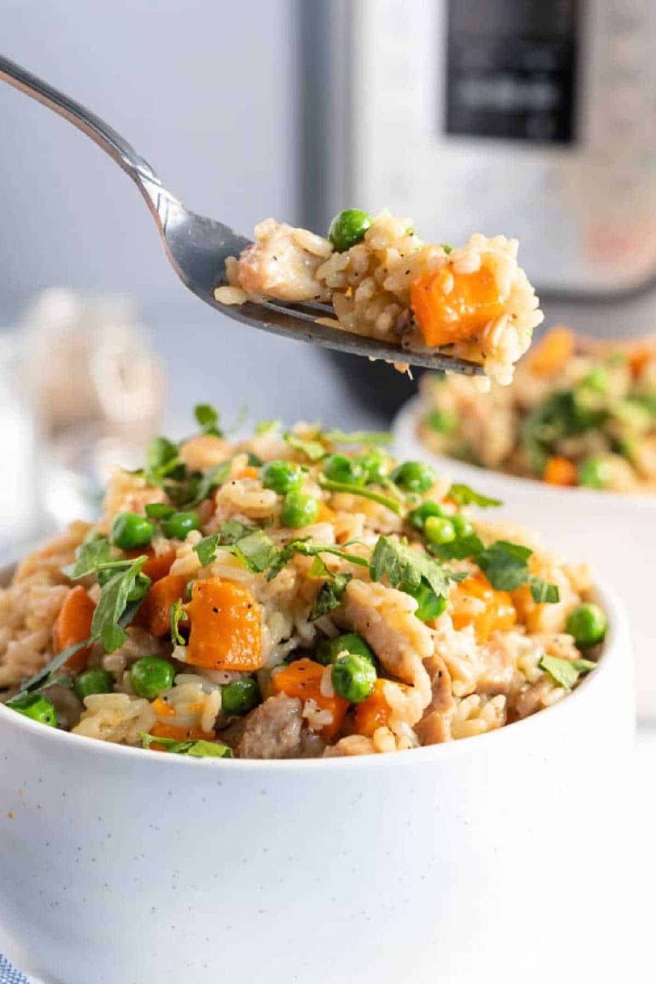 A bowl of instant pot chicken thighs and rice with peas, carrots, and herbs, as a fork lifts a good bite above it.