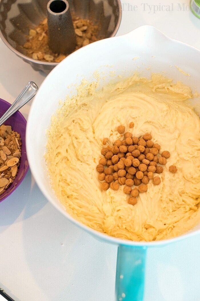 Cake batter with butterscotch chips in a mixing bowl, solid for making an instant pot coffee cake, with a purple bowl and bundt pan in the background.