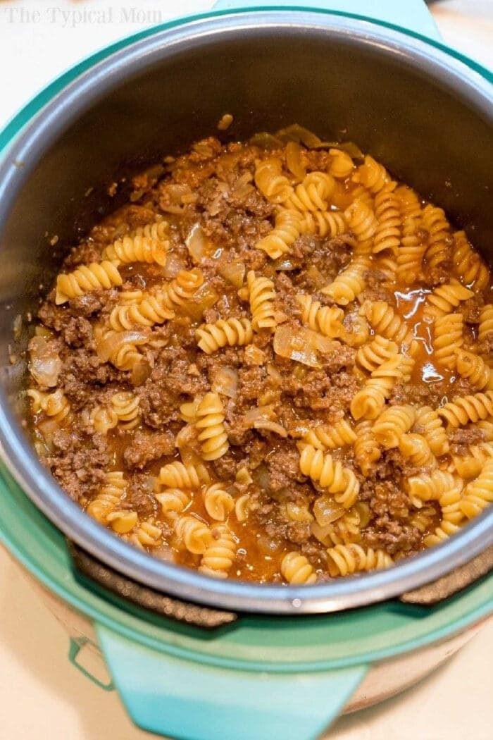 Cooked rotini pasta with ground beef and sauce in a teal pressure cooker, solid for making a quick instant pot enchilada casserole.