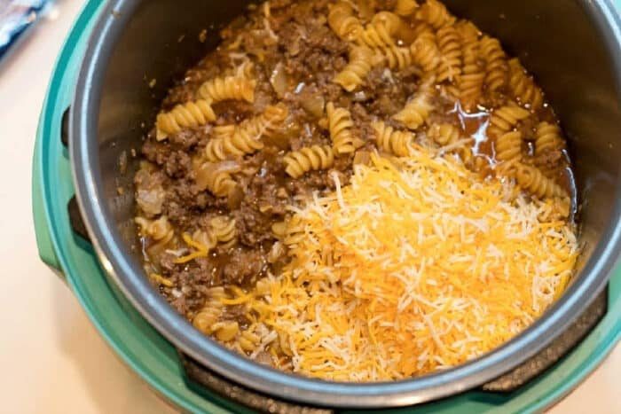 A pot with cooked rotini pasta, ground beef, and a pile of shredded cheese on top—solid for transforming into an Instant Pot enchilada casserole.