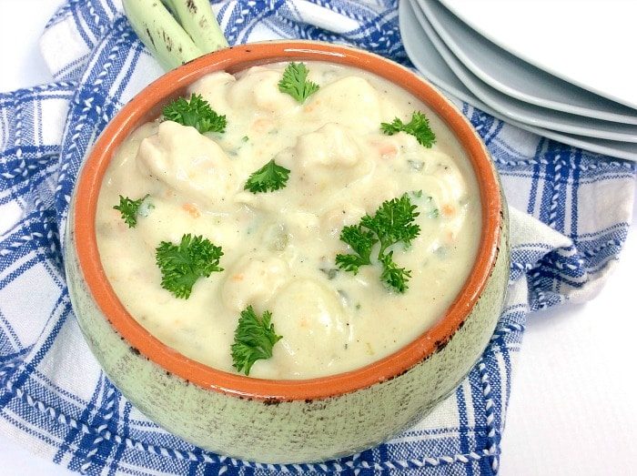 A ceramic bowl of creamy instant pot gnocchi soup garnished with parsley sits gracefully on a blue and white checkered cloth, surrounded by neatly stacked plates in the background.