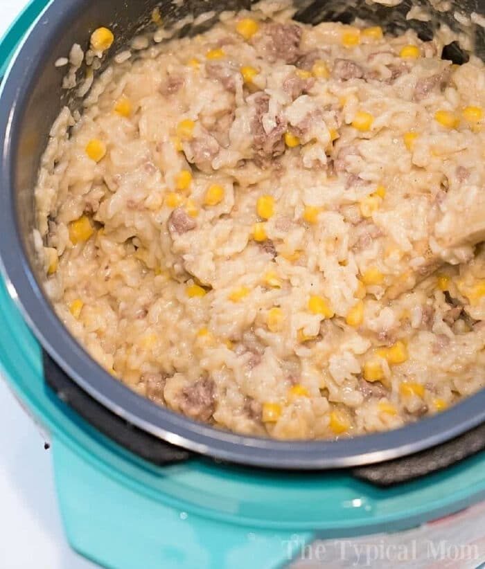 Creamy rice, ground beef, and corn mixture being stirred in a blue rice cooker—a good take on instant pot hamburger casserole.