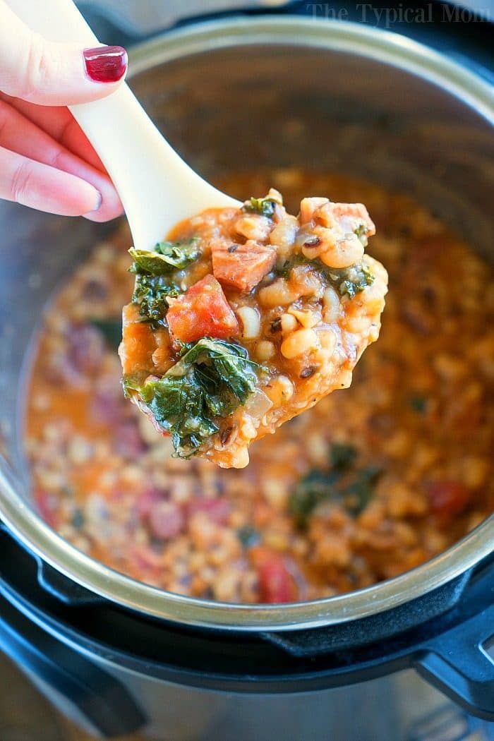 Close-up of a ladle with hoppin john featuring tomatoes and greens, held over an Instant Pot.
