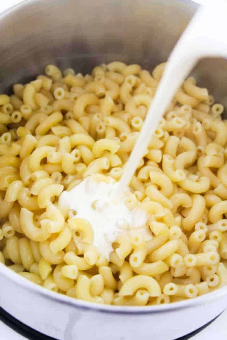 A pot of cooked instant pot macaroni and cheese with milk being poured over it, ready for mixing.