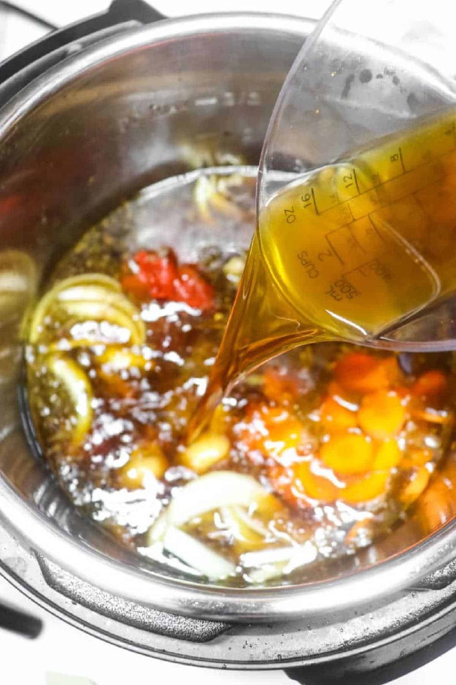 Olive oil is being poured into an Instant Pot with sliced onions, carrots, and tomatoes, creating a savory base for Instant Pot Oxtail Soup.