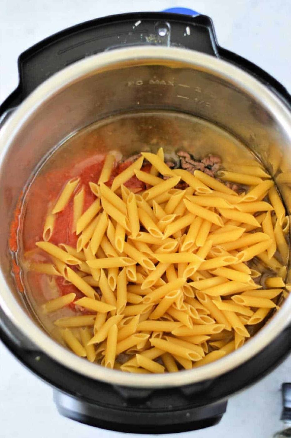 Uncooked instant pot penne pasta, ground meat, and tomato sauce are combined in the Instant Pot, ready to be cooked for a quick and good meal.