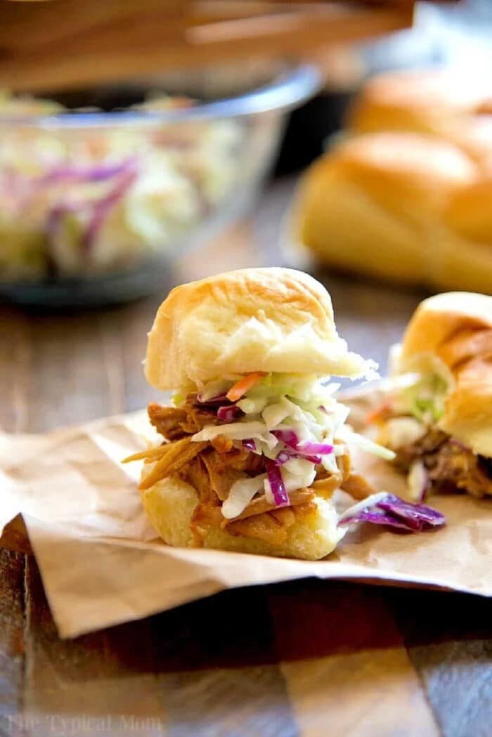Pulled pork slider topped with coleslaw on a bun, made using an instant pot pork shoulder recipe, placed on parchment paper with more sliders in the background.