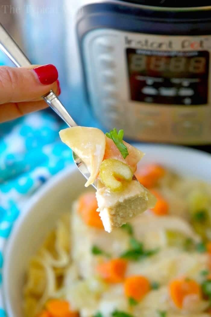 A fork holds chicken, noodles, and carrots above a bowl, with an Instant Pot in the background—solid for trying your favorite instant pot pork stroganoff recipe.