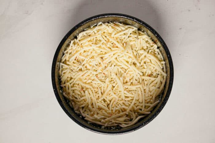 A black bowl filled with shredded cheese on a white marble surface, solid for adding to your favorite Quiche or Instant Pot Quiche recipe.