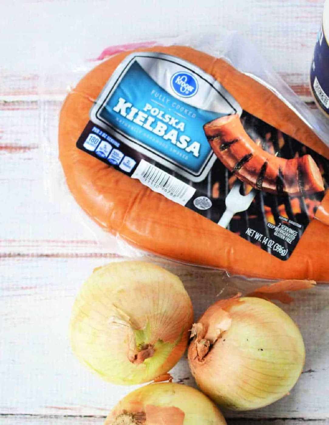 Packaged Polska kielbasa sausage next to three yellow onions on a light wooden surface—solid ingredients for making instant pot red beans and rice.