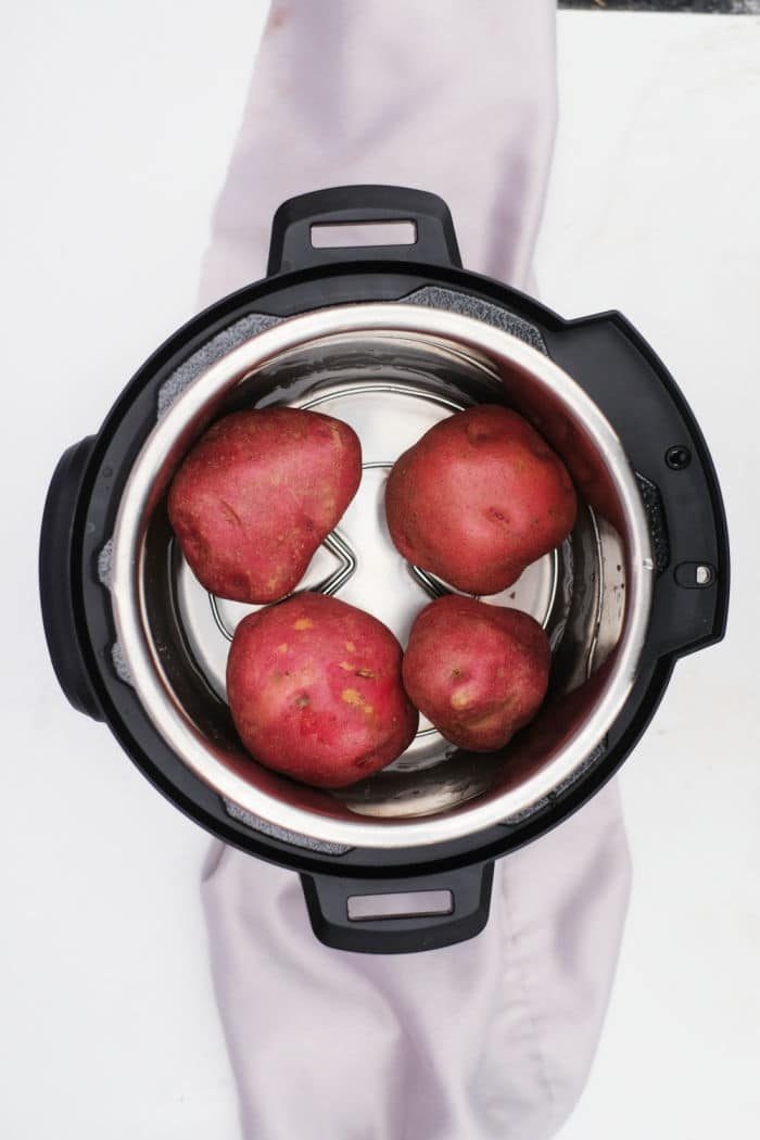 Overhead view of four Instant Pot Red Potatoes inside an electric pressure cooker on a white surface.