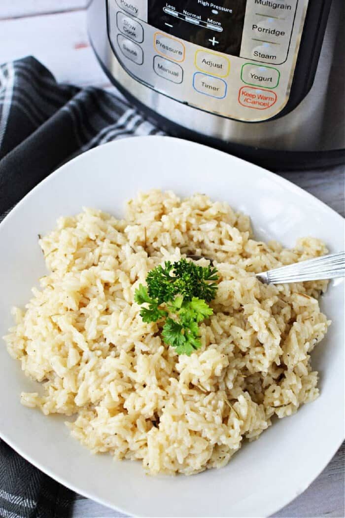 A plate of cooked risotto garnished with parsley sits next to an Instant Pot, showcasing a good instant pot risotto recipe, with a fork placed on the plate for easy serving.