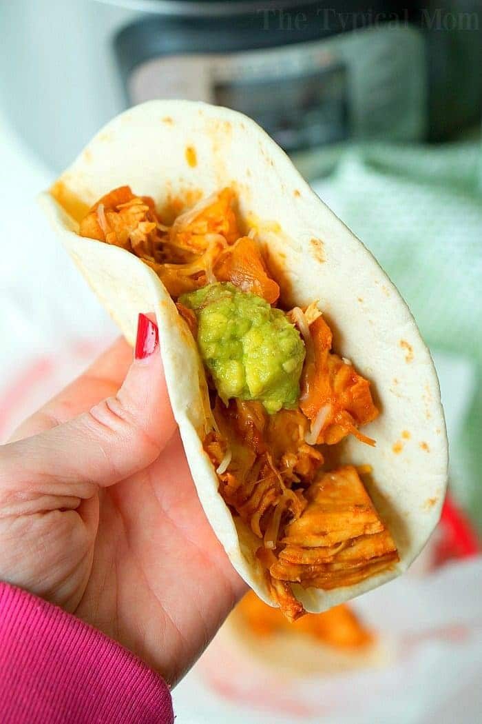 A hand holds a taco filled with guacamole and savory instant pot shredded chicken, offering a good bite.