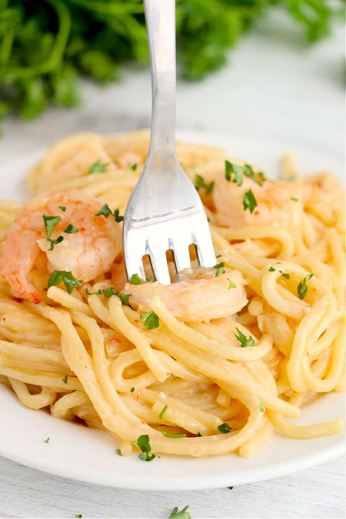 Fork in creamy shrimp pasta garnished with parsley on a white plate, reminiscent of the flavors of instant pot bang bang shrimp.