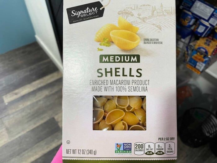 Box of Signature Select medium shells pasta, an enriched macaroni product made with 100% semolina, solid for dishes like instant pot sloppy joe casserole. Includes nutrition facts: 200 calories per serving, non-GMO verified. Box design features pasta image and Tuscany-inspired illustration. Net weight 12 oz.