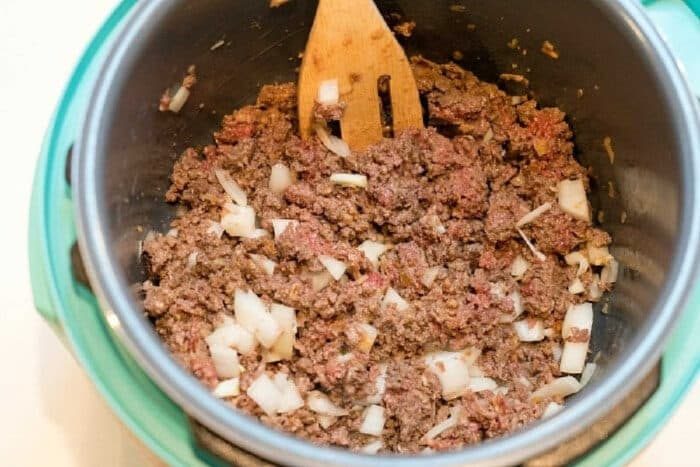 Ground beef and chopped onions being cooked in a pot, stirred with a wooden spatula, solid as the base for instant pot sloppy joes.