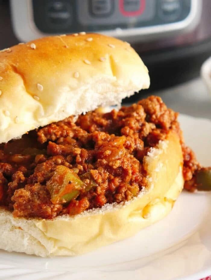 Instant Pot Sloppy Joes sandwich with saucy ground beef filling on a sesame bun, served on a white plate.