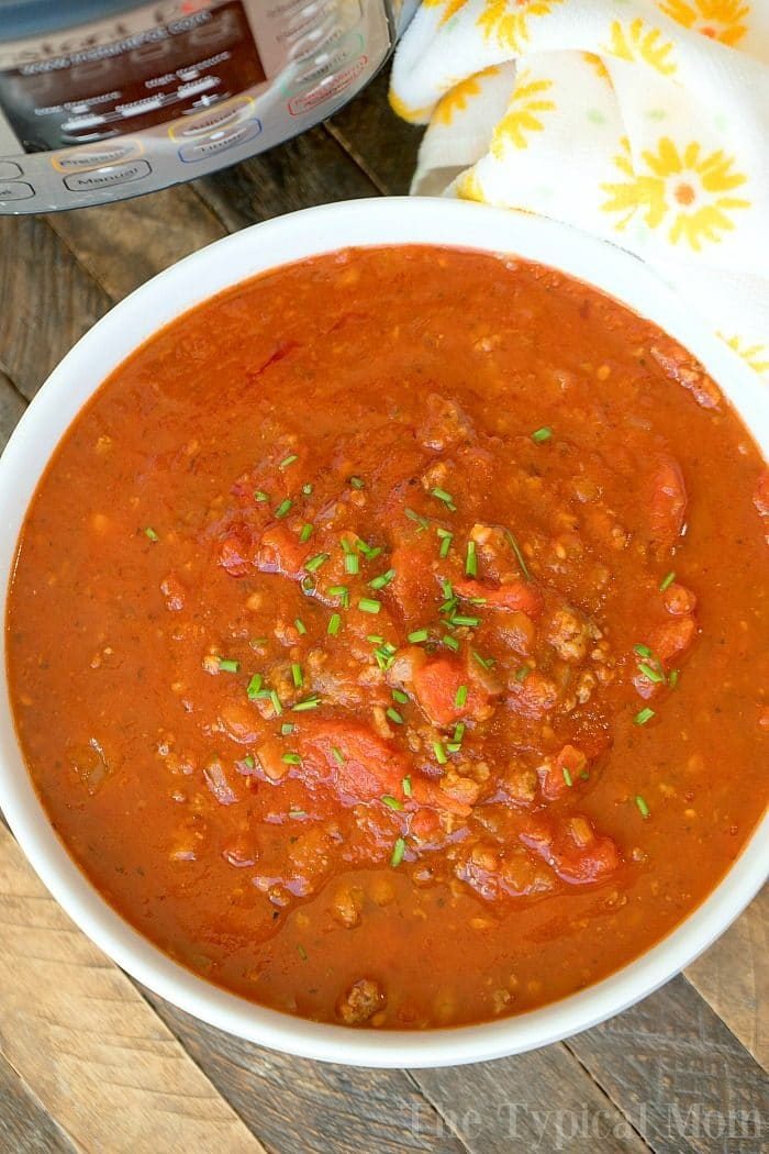 A bowl of hearty spaghetti sauce garnished with herbs sits next to an Instant Pot, ready to whip up a good spaghetti sauce, all on a rustic wooden surface.