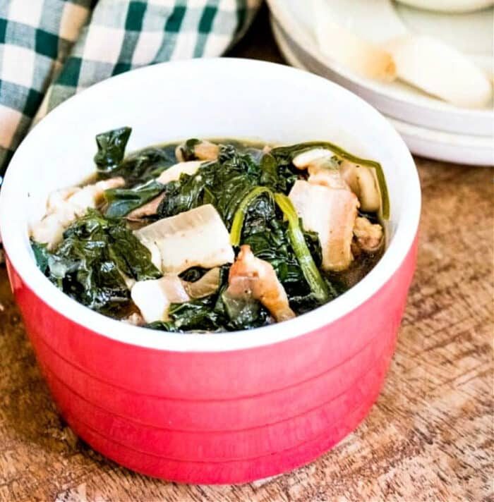 A bowl of spinach sits on a wooden table, steaming beside a checkered cloth, ready to enjoy from the instant pot.