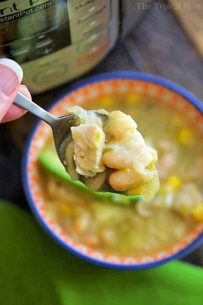 A spoonful of Instant Pot white chicken chili held above a bowl, with the pressure cooker in the background.