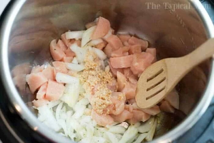 Chopped raw chicken, onions, and minced garlic in a pot with a wooden spoon—solid for starting your instant pot white chicken chili.