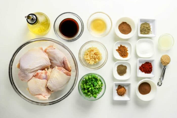 Raw chicken thighs, chopped green onions, minced garlic, sauces, oil, and various spices arranged on a white surface—solid for preparing flavorful Oven Jerk Chicken.