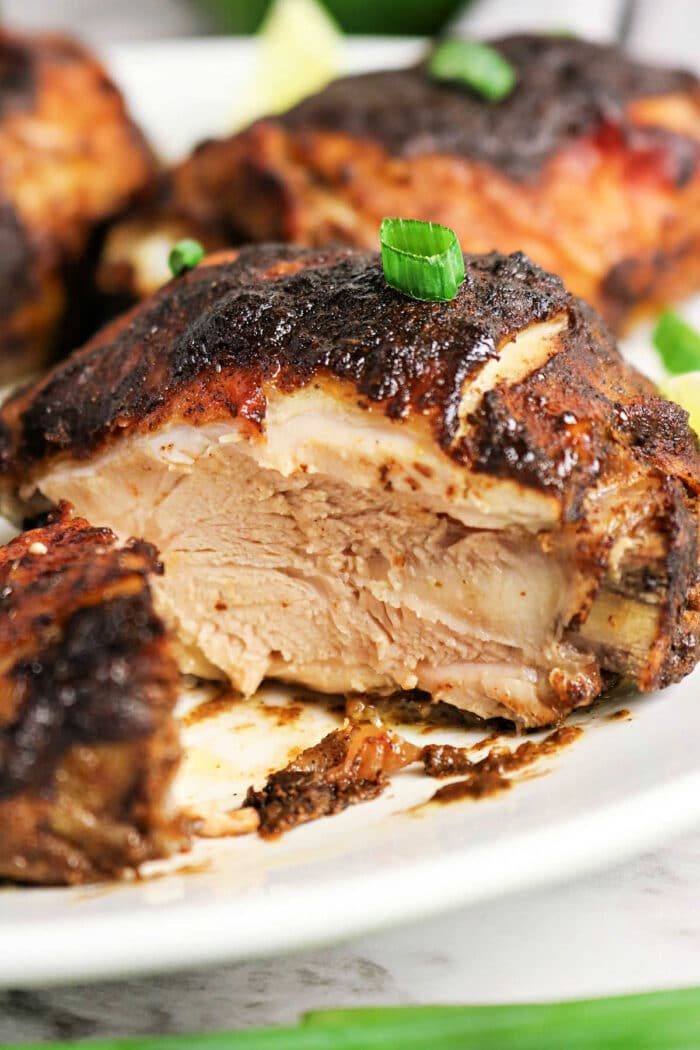 A close-up of juicy, oven jerk chicken with crispy, seasoned skin, garnished with chopped green onions.
