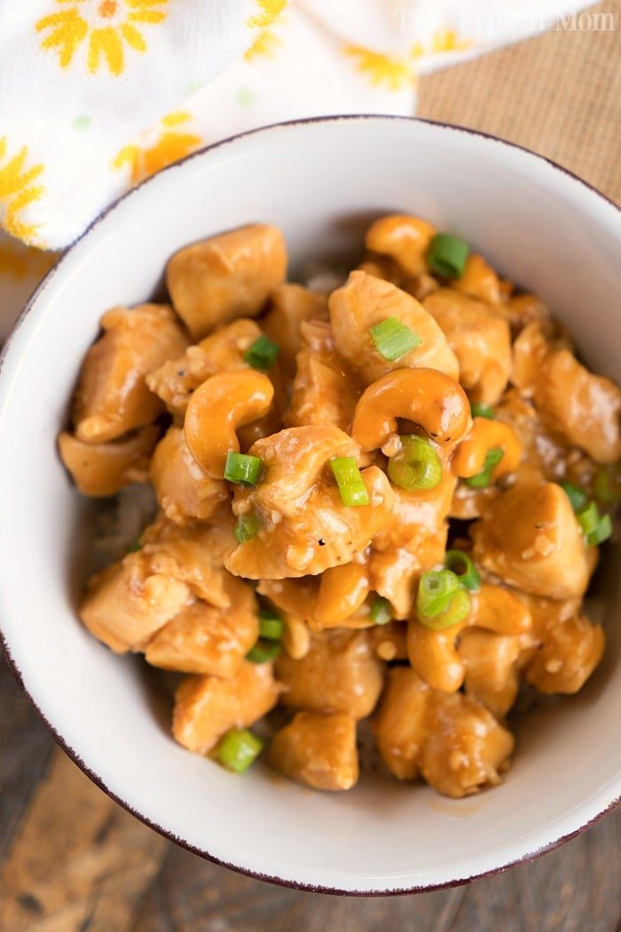A bowl of pressure cooker cashew chicken, garnished with green onions, rests enticingly on a wooden table.
