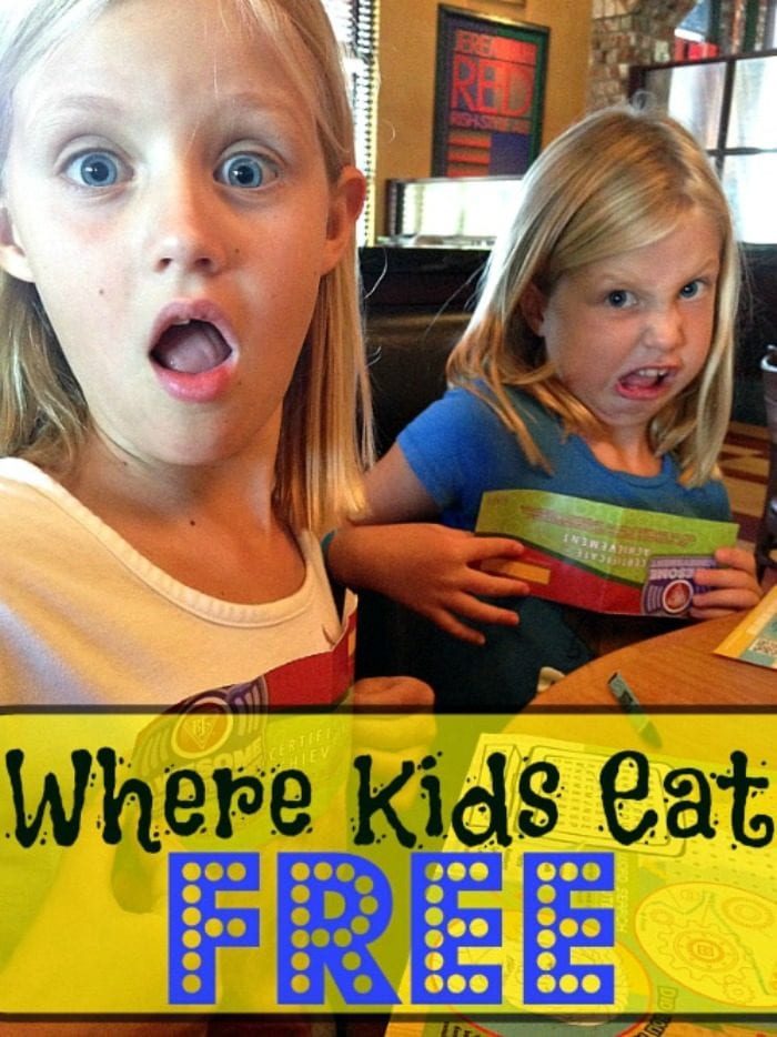 Two young girls with surprised expressions sit at a table in a bustling restaurant. One is dressed in a crisp white shirt, while the other sports a cheerful blue one. A yellow banner below proudly announces this as the place where kids eat free, adding to their joy.