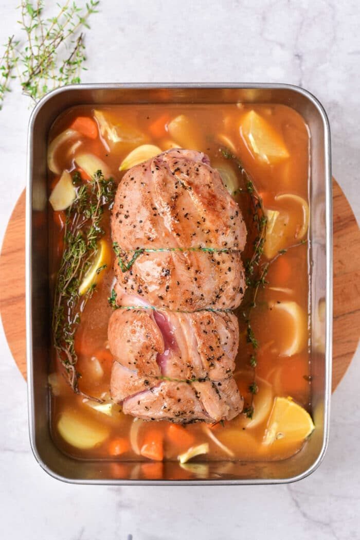Roasted lamb breast in a pan, accompanied by carrots, potatoes, and herbs on a wooden board. For those seeking variation, consider exploring a tender lamb breast recipe that pairs beautifully with similar earthy accompaniments.