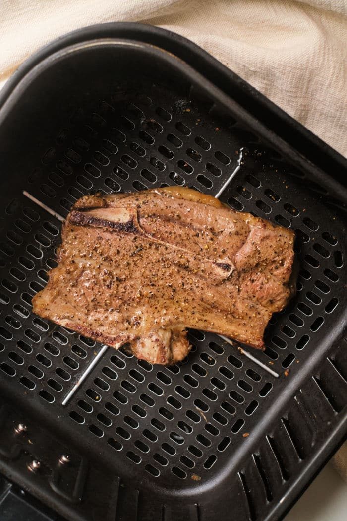 Perfectly cooked lamb chops in an air fryer basket, set against a light fabric background.