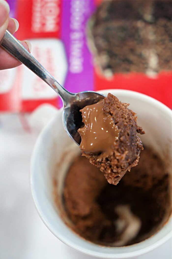 A spoon holds chocolate cake with a molten center above a white cup and cake mix box—solid for your next Lava Cake Recipe or quick Mug Cake craving.