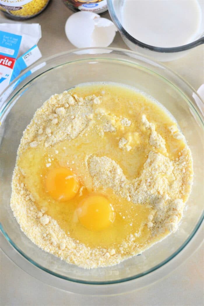 On a kitchen counter, a bowl filled with cornbread mix, two eggs, and melted butter sits among baking ingredients. Get creative with leftover cornbread recipes by mixing these basics into delightful treats.
