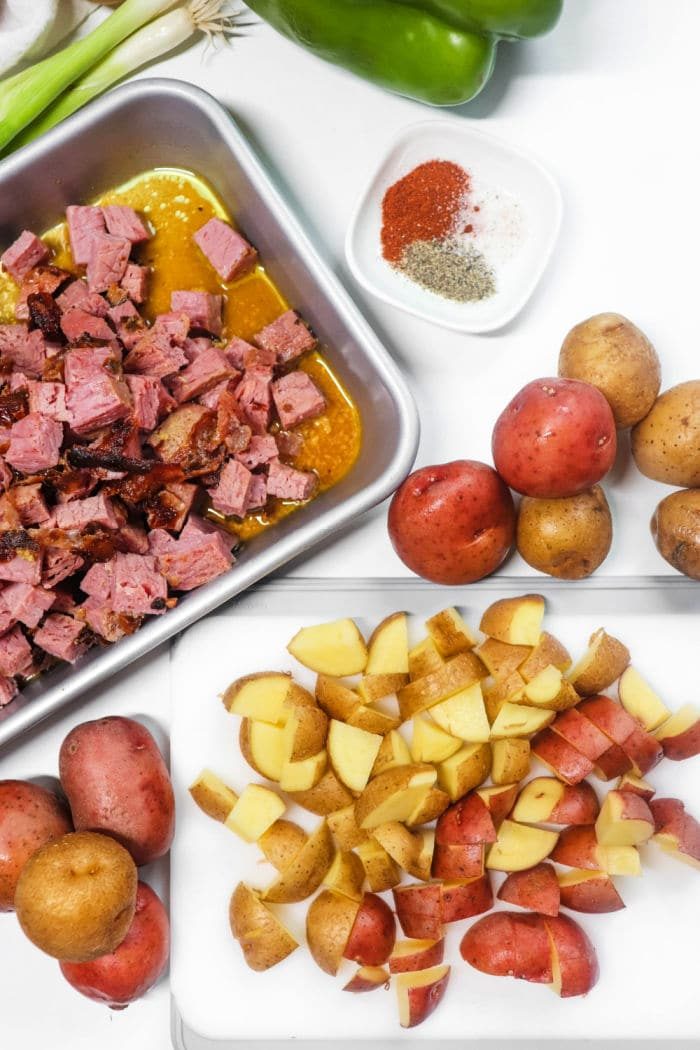 Chopped corned beef meat in a tray, diced potatoes on a cutting board, with spices and vegetables around—solid for creating an Air Fryer Corned Beef Hash with tender red potatoes.