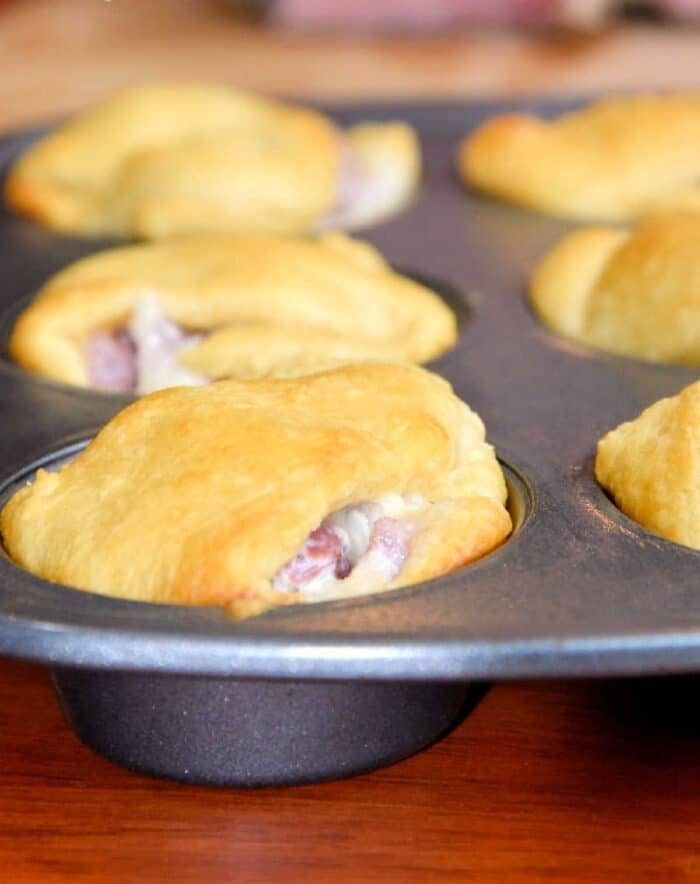 Golden brown crescent roll sandwiches baked in a muffin tin, with filling visible at the edges—a solid leftover ham recipe for easy, savory snacks.