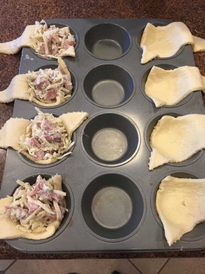 Muffin tray with unbaked crescent rolls filled with a delightful cheese and leftover ham mixture.