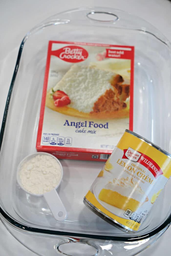 A glass baking dish with angel food cake mix, lemon creme pie filling, and a measuring cup of flour—solid for preparing dessert after trying a new Carnivore Meatloaf or your favorite meatloaf recipe.
